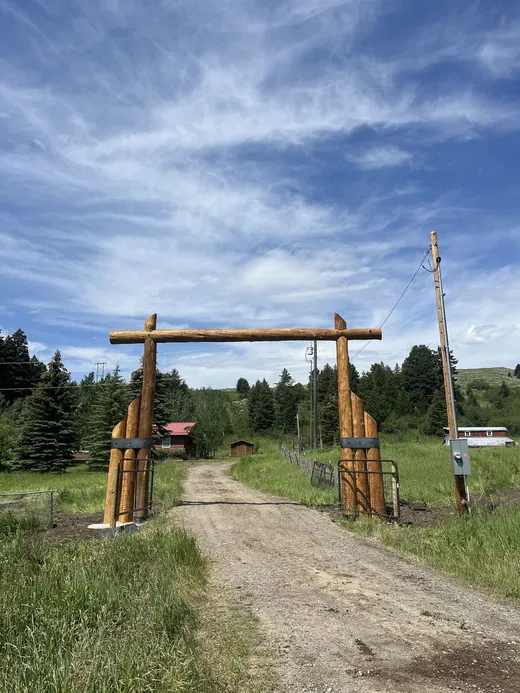 Log ranch archway with steel-banded stacked-log columns at Quinn Creek, Montana